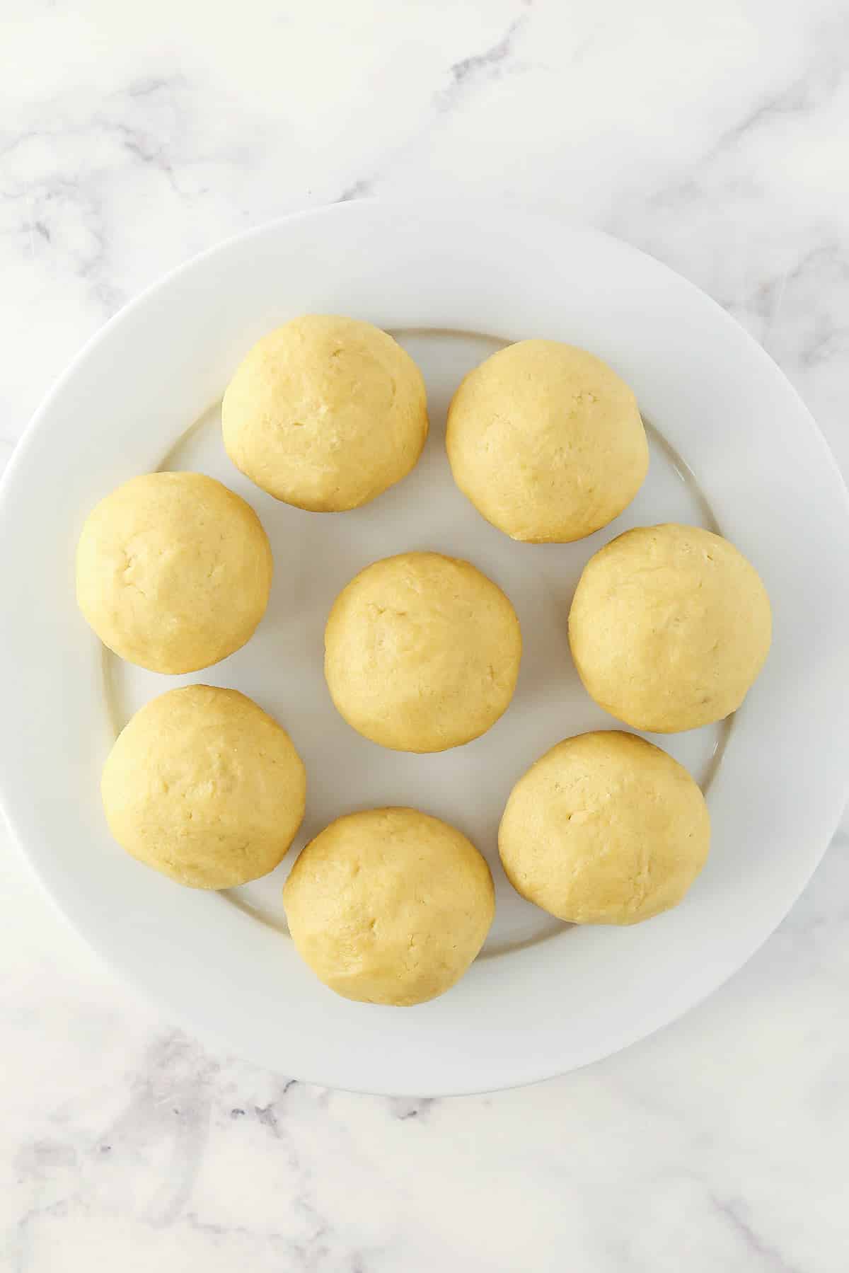 Eight large balls of sugar cookie dough on a round plate