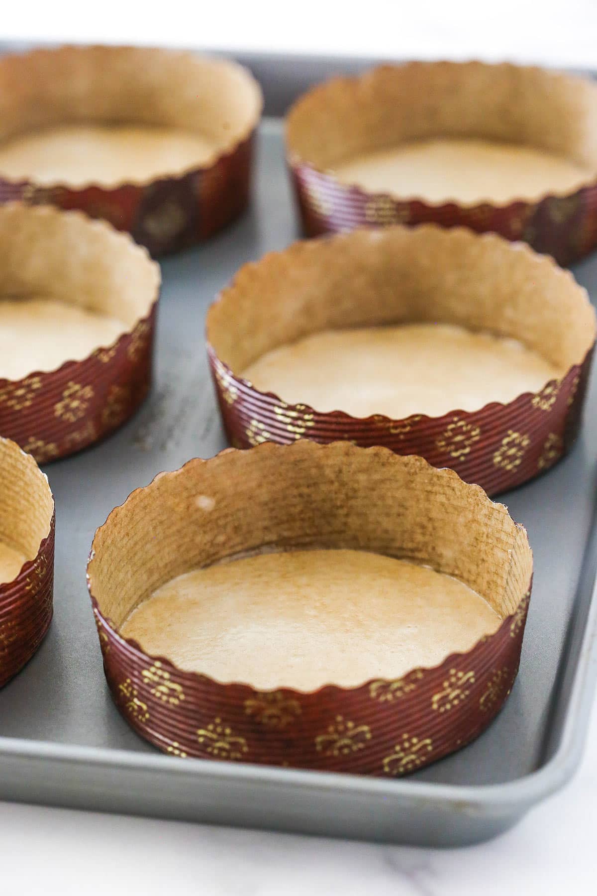 Paper pie pans lined up on a baking sheet on top of a marble counter