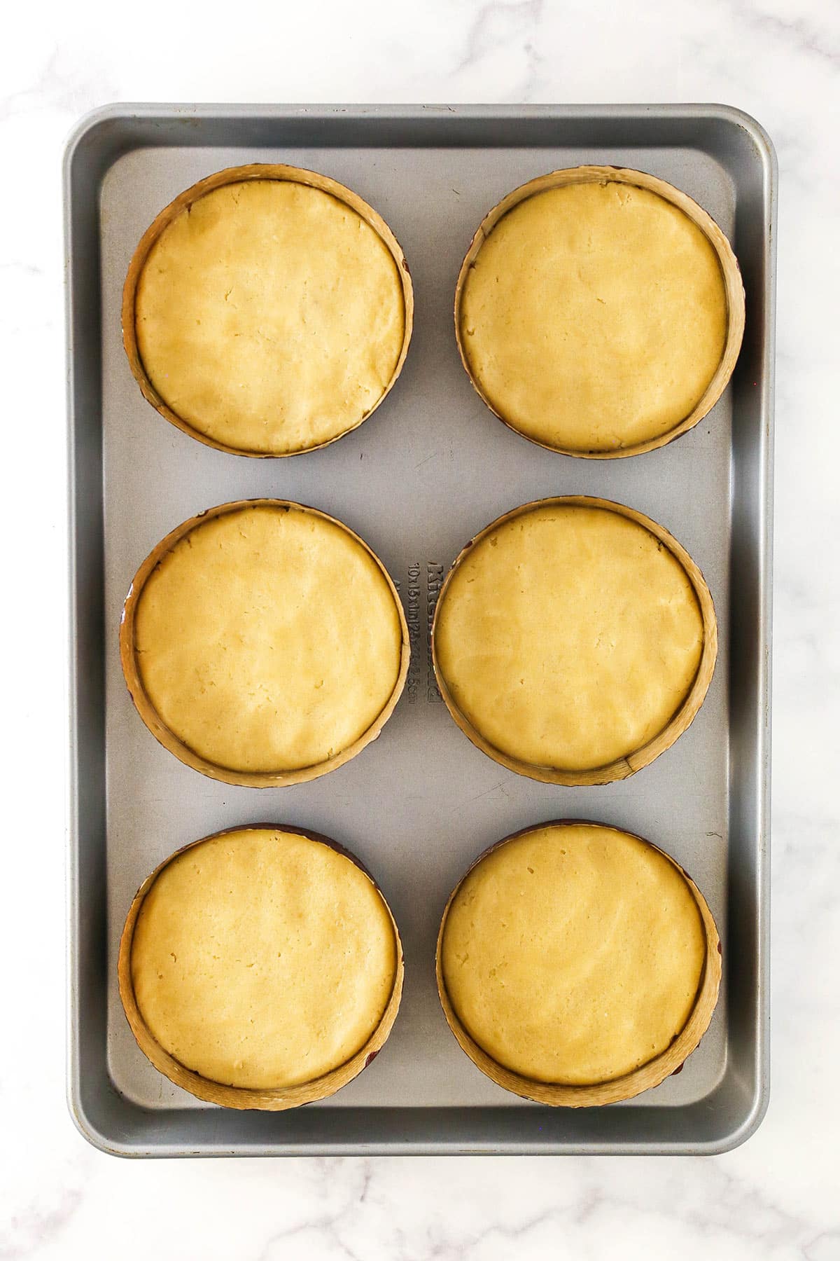 Sugar cookie dough pressed into six paper pie pans on a silver baking sheet