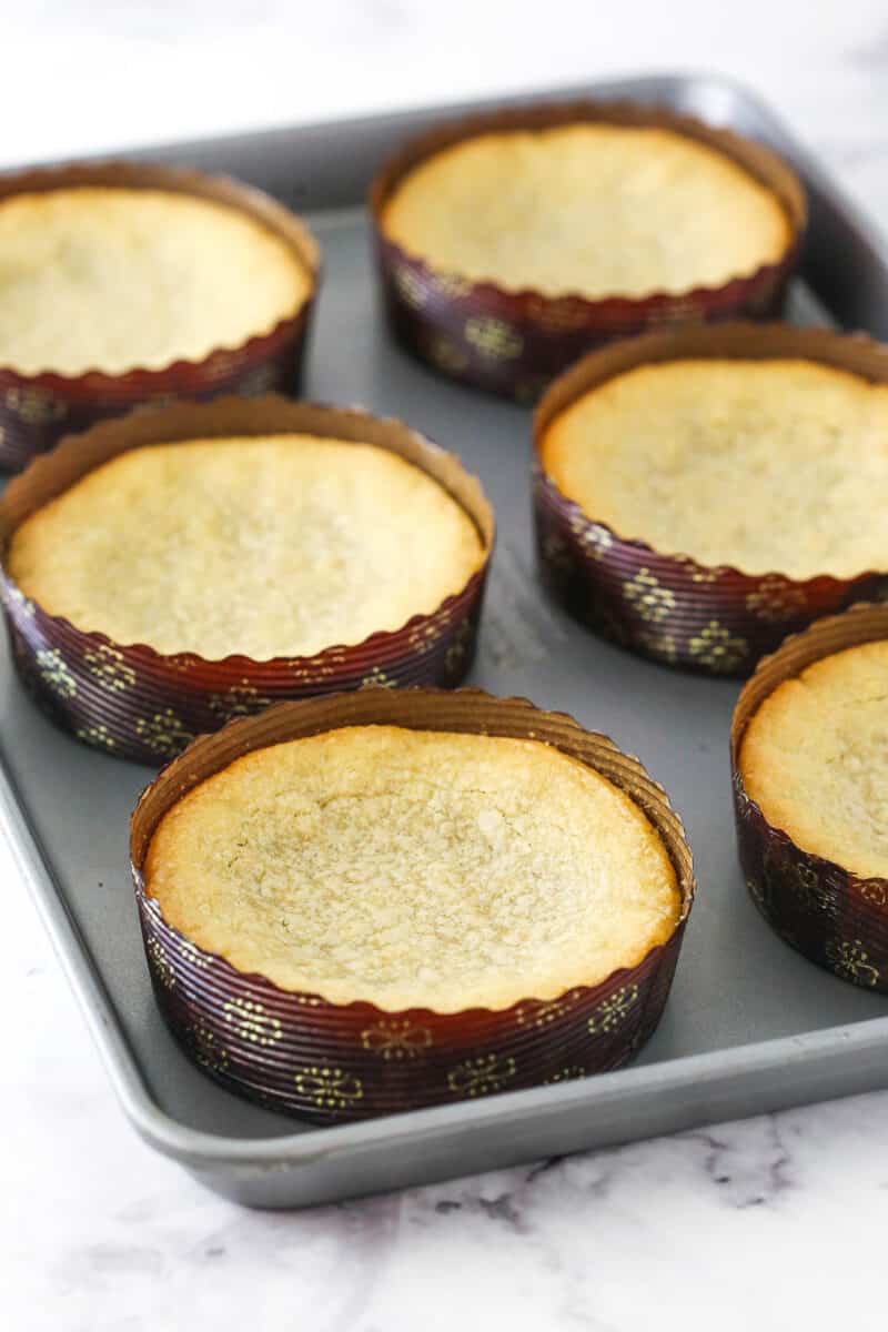A baking sheet holding six large sugar cookies inside of paper pie pans