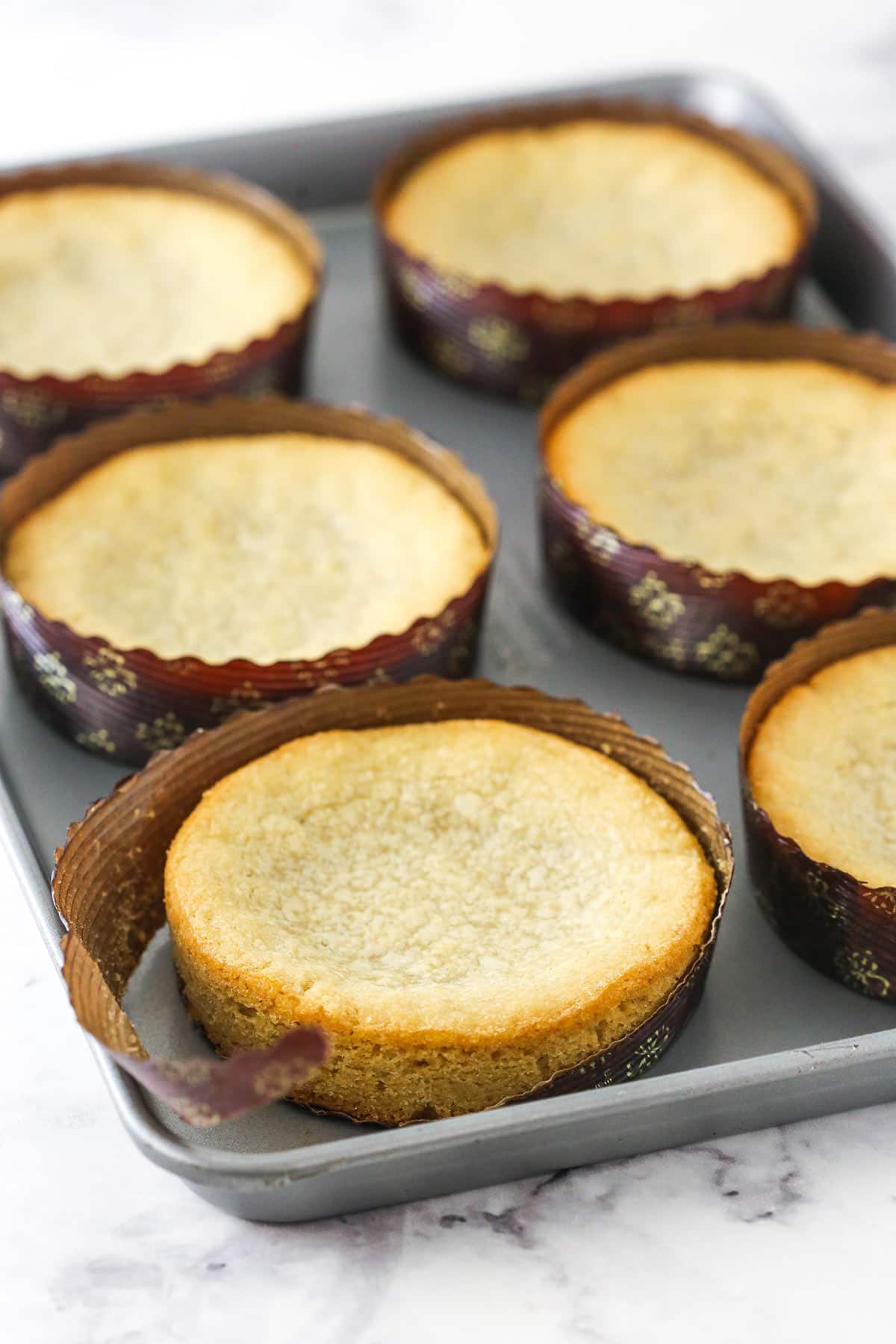 Six big sugar cookies in paper pie pans with one of the paper pans peeled off