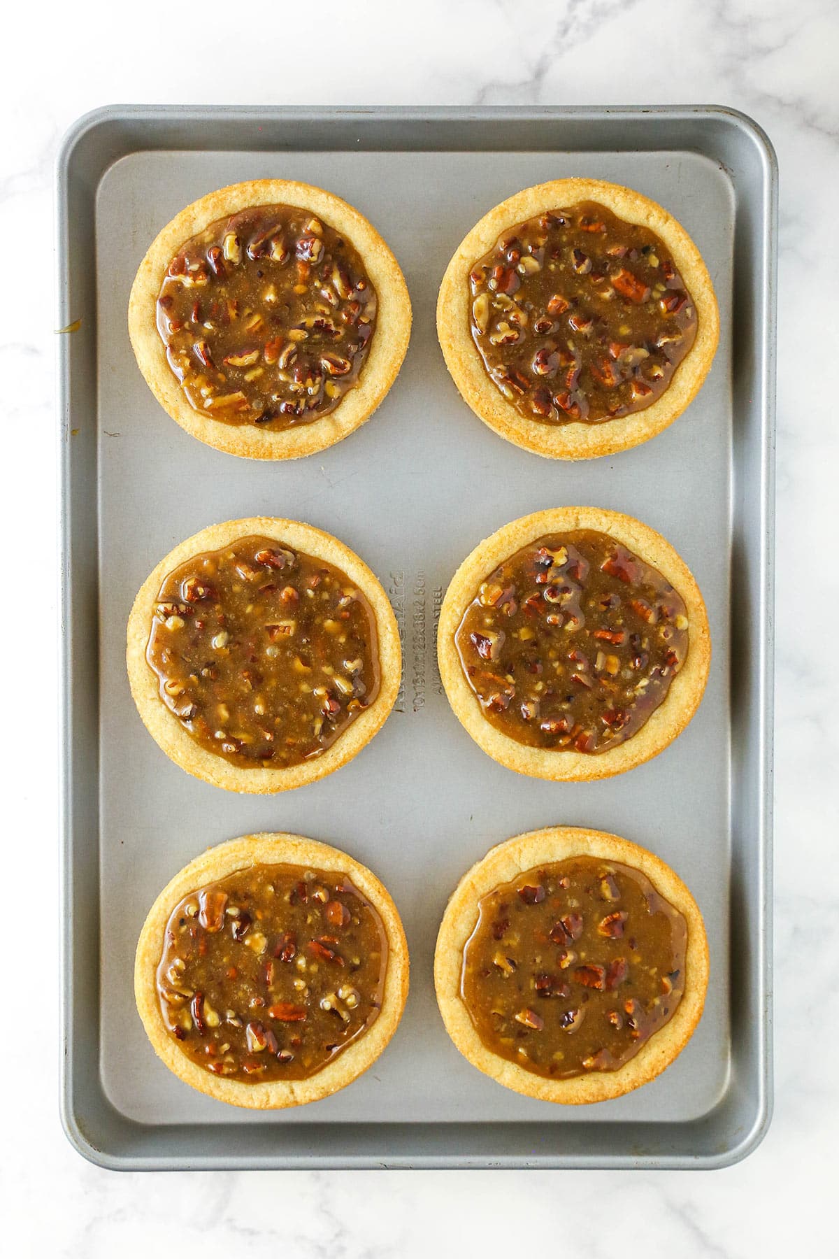 Six pecan pie cookies on a metal baking sheet on top of a kitchen counter