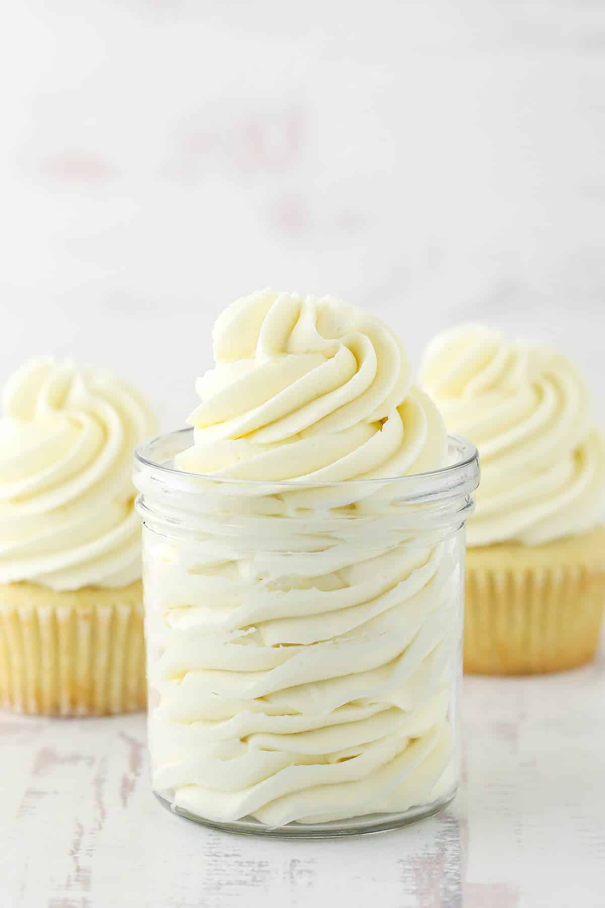 ermine frosting piped into glass jar with two frosted cupcakes in the background