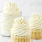 two frosted cupcakes and jar of frosting on white background