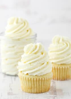 two frosted cupcakes and jar of frosting on white background