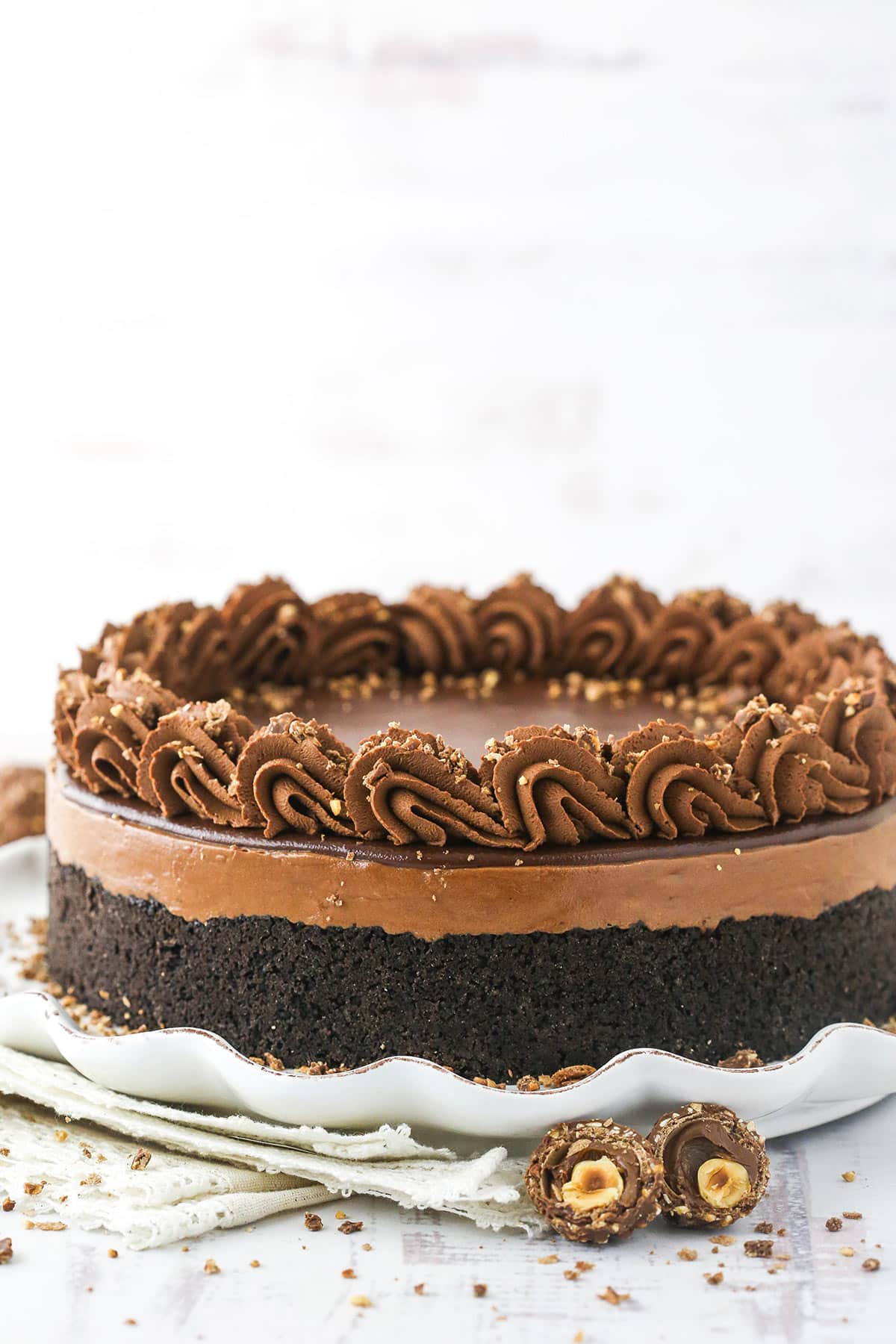 A chocolate hazelnut cheesecake on a kitchen countertop beside a halved Ferrero Rocher chocolate