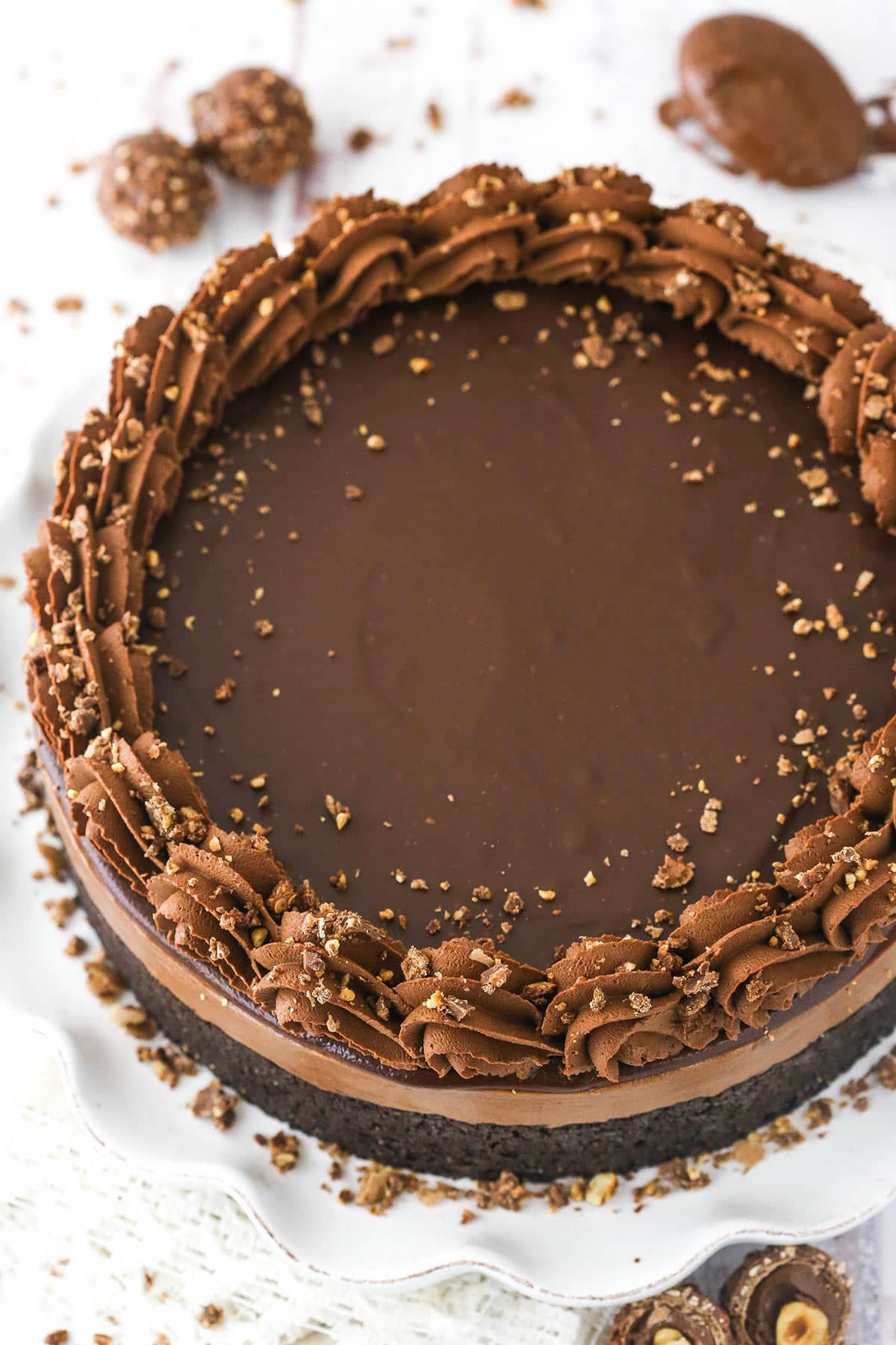 An overhead shot of a chocolate hazelnut cheesecake on a serving platter with a spoonful of chocolate hazelnut spread beside it