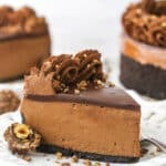 A piece of chocolate hazelnut cheesecake on a plate with a second piece and the remaining cake behind it