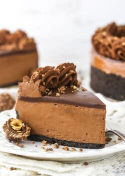 A piece of chocolate hazelnut cheesecake on a plate with a second piece and the remaining cake behind it