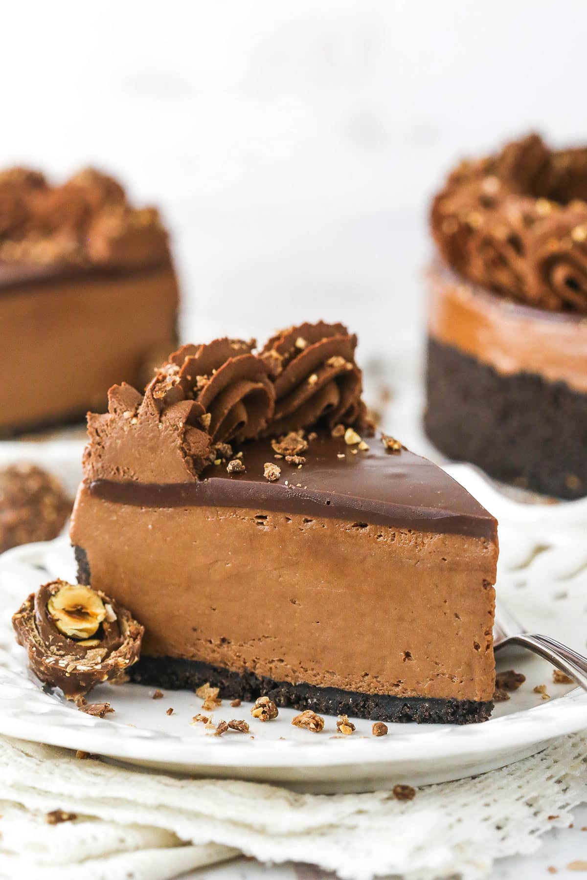 A piece of chocolate hazelnut cheesecake on a plate with a second piece and the remaining cake behind it