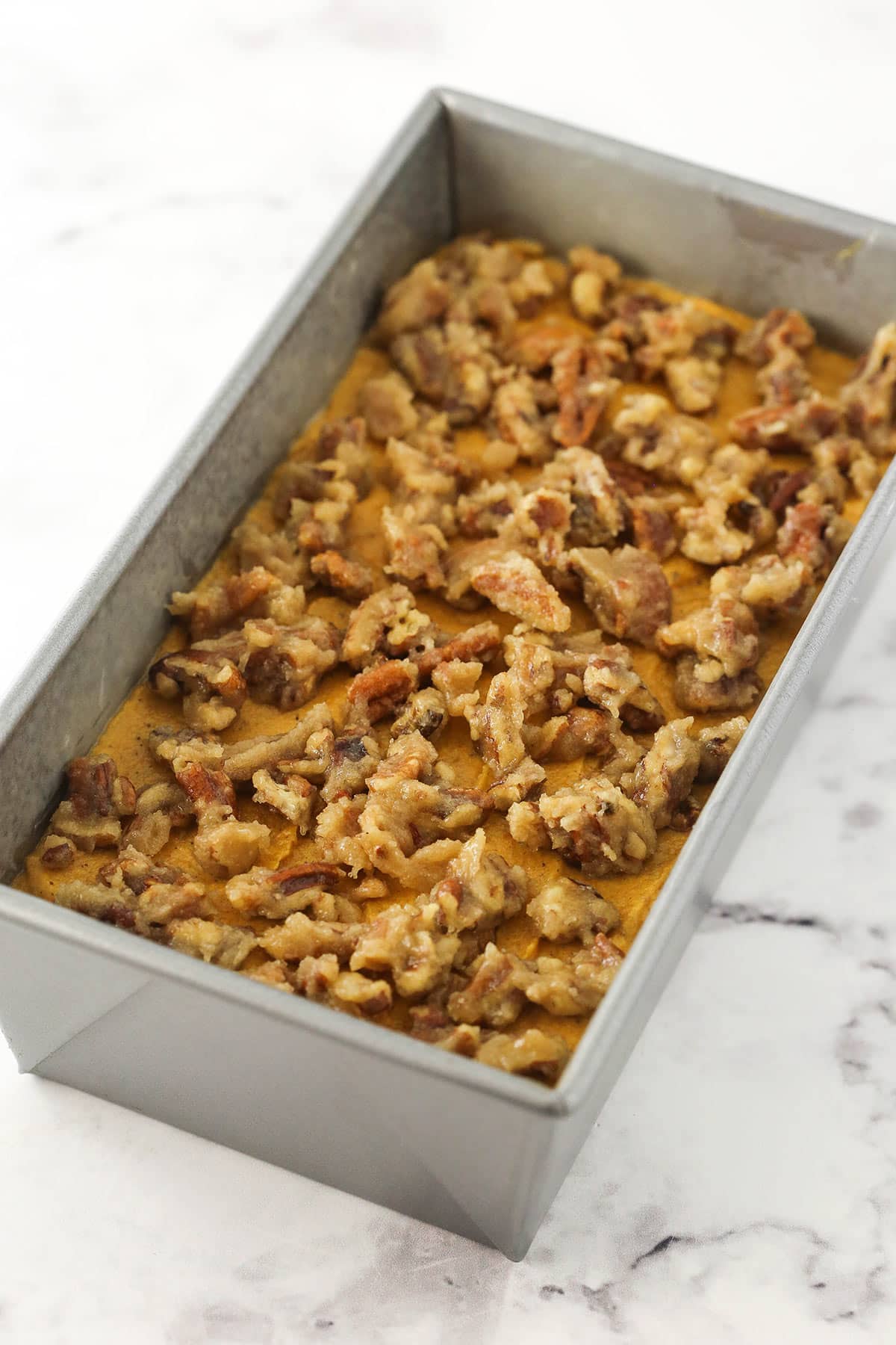 Layers of pumpkin bread batter and pecan praline filling in a metal loaf pan