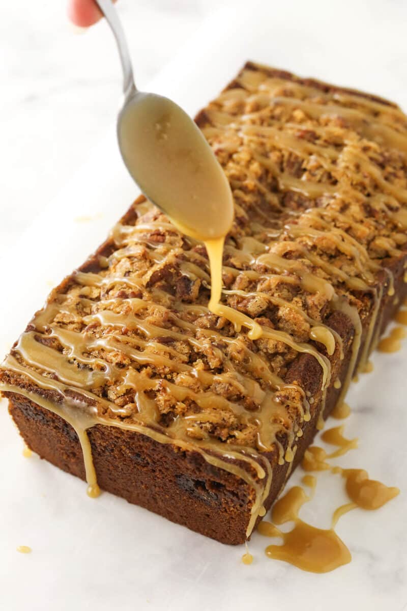 Brown sugar glaze being drizzled over a loaf of pecan praline pumpkin bread