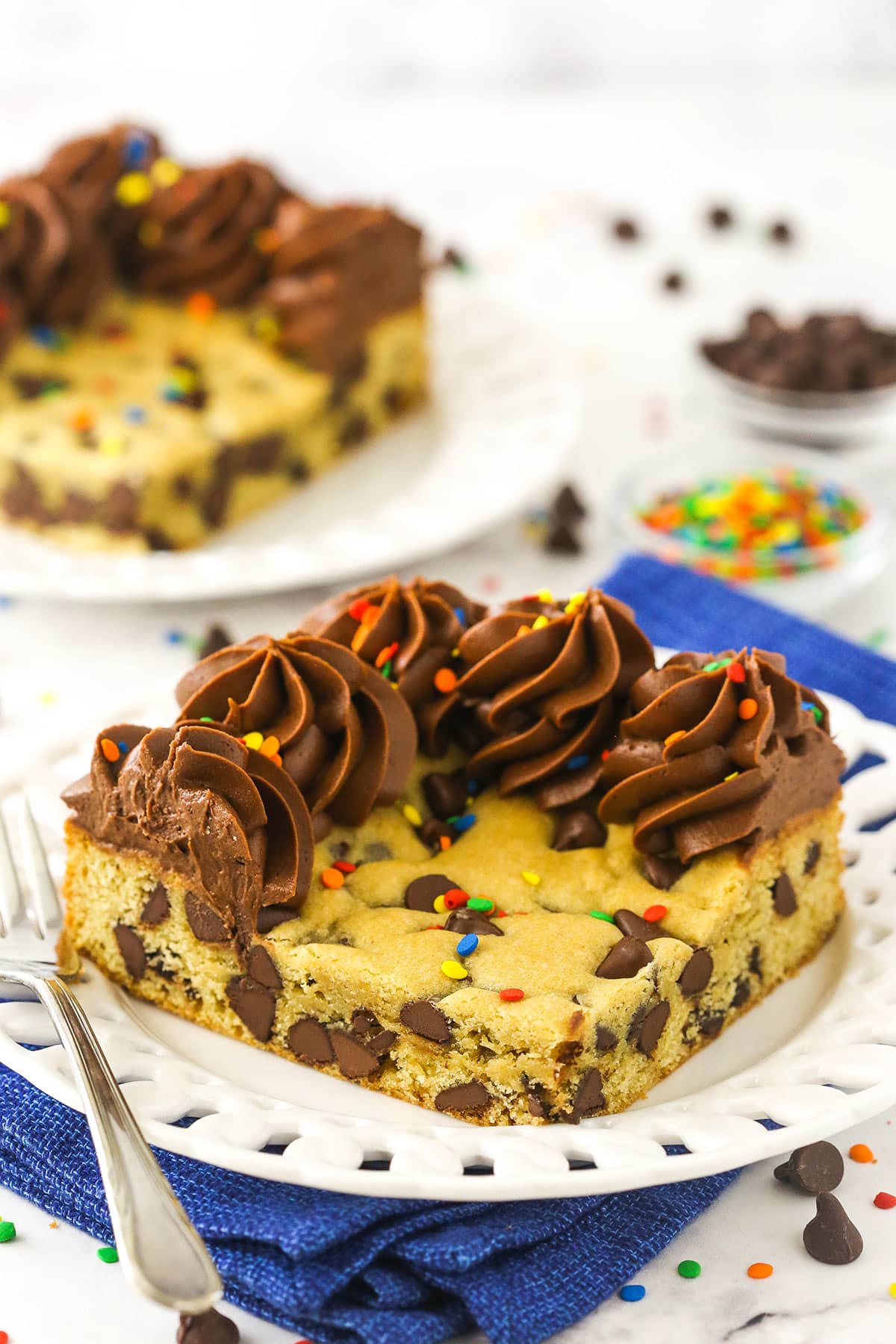 A white dessert plate holding a big slice of chocolate chip cookie cake