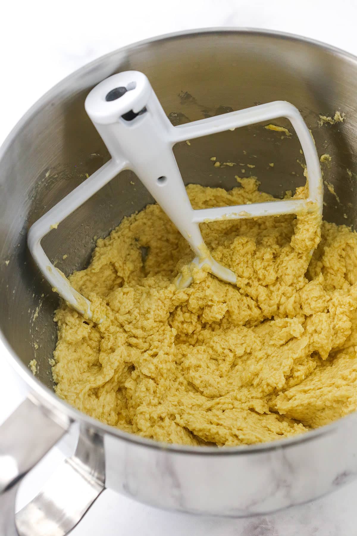 In-progress chocolate chip cookie dough inside of a large metal mixing bowl