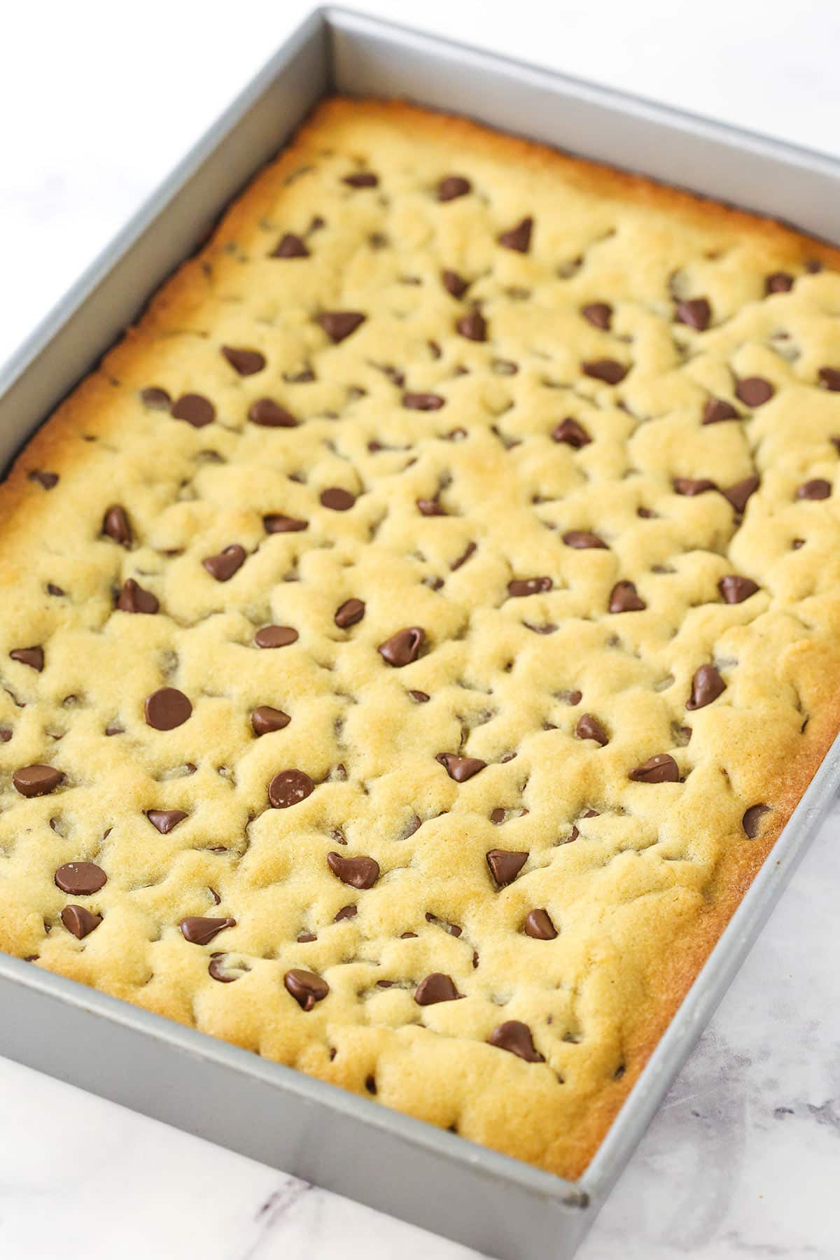 A chocolate chip cookie cake inside of a metal sheet pan on a kitchen countertop