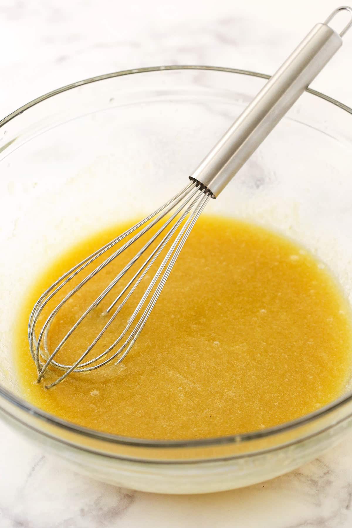 The combined wet ingredients inside of a glass mixing bowl with a metal whisk