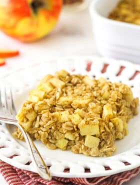 A square of apple cinnamon baked oatmeal on a white plate on top of a red and white striped dishtowel