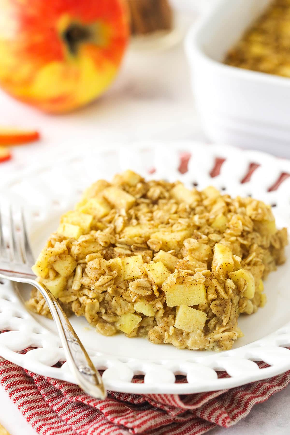 A square of apple cinnamon baked oatmeal on a white plate on top of a red and white striped dishtowel