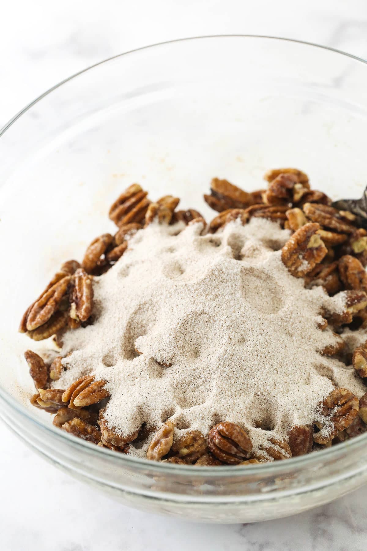 A bowl of pecans coated in whipped egg whites with cinnamon sugar poured on top
