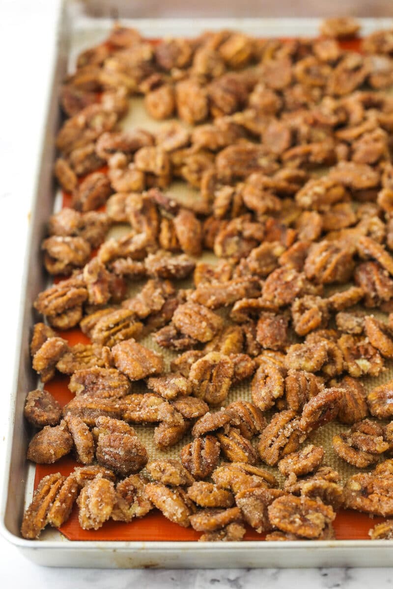 Unbaked candied pecans on a lined baking sheet on top of a marble counter.