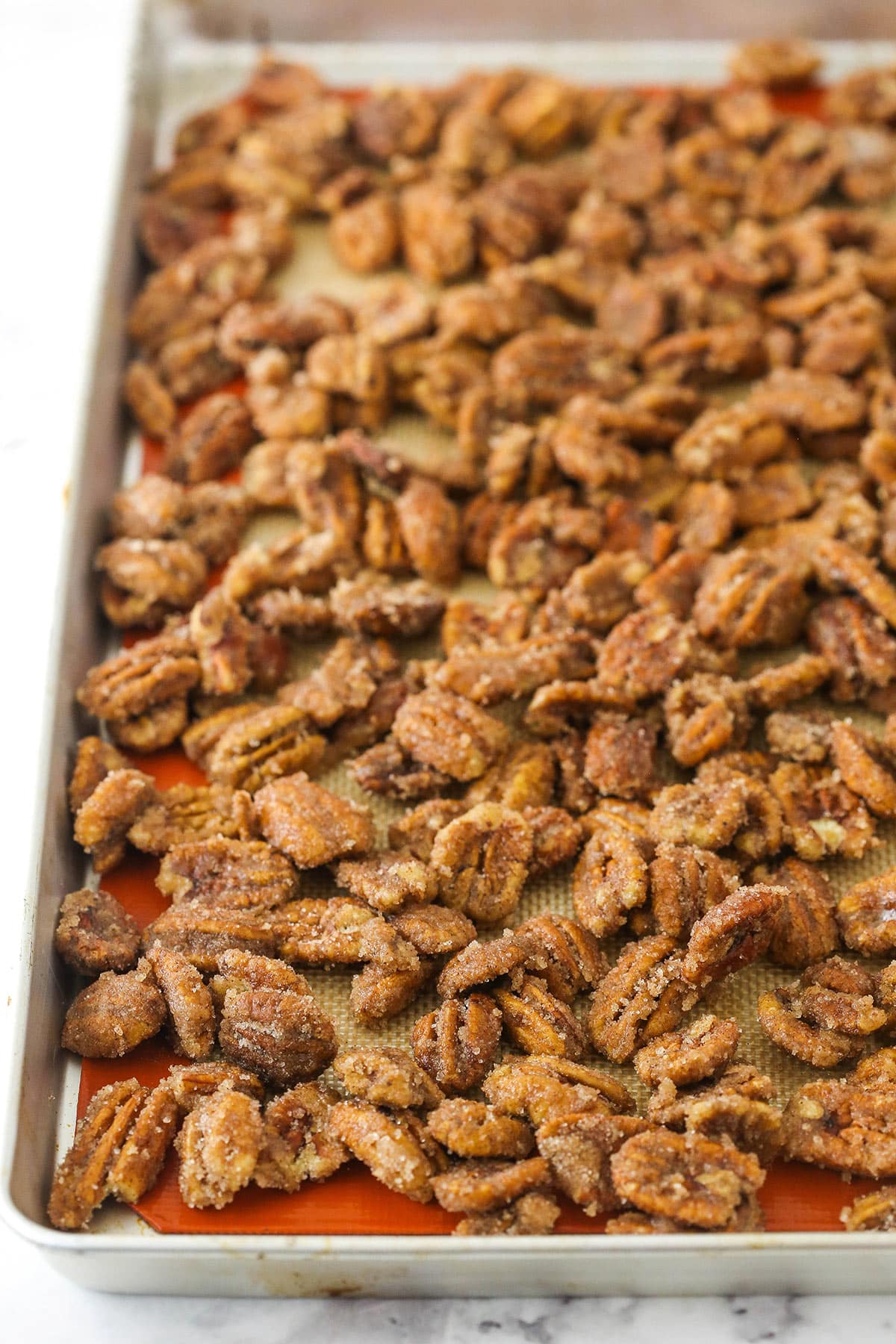 Unbaked candied pecans on a lined baking sheet on top of a marble counter