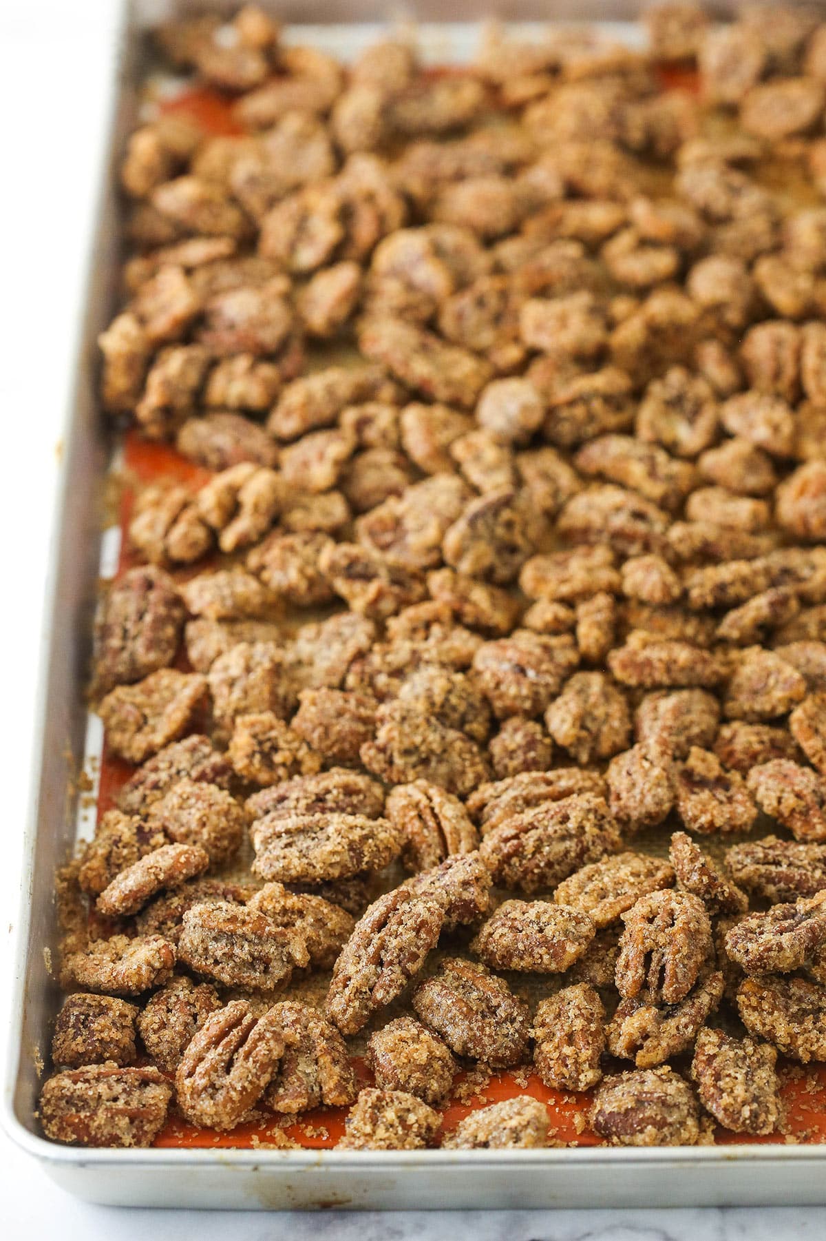Freshly baked cinnamon sugar pecans on a lined baking sheet with a raised rim