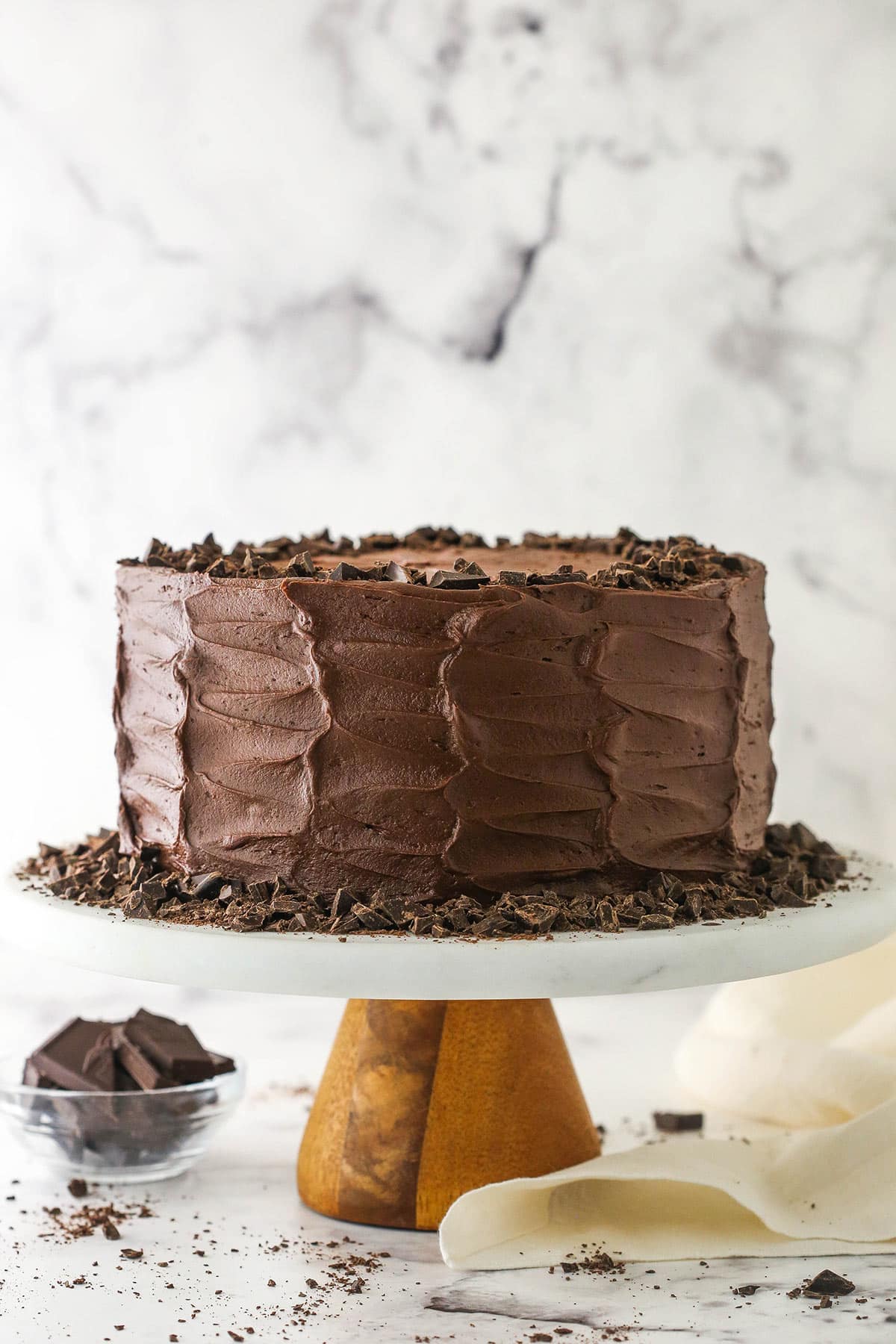 fully frosted Devil's Food Cake on marble stand with bowl of chocolate and cream cloth in background