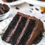 slice of Devil's Food Cake on white plate with another slice and bowl of chocolate in the background