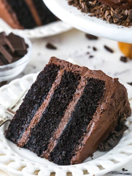 slice of Devil's Food Cake on white plate with another slice and bowl of chocolate in the background