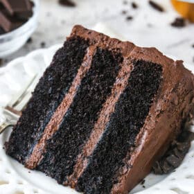 slice of Devil's Food Cake on white plate with another slice in the background on a marble table