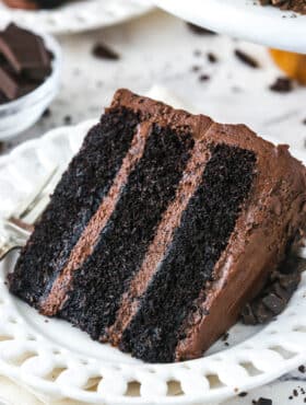 slice of Devil's Food Cake on white plate with another slice in the background on a marble table