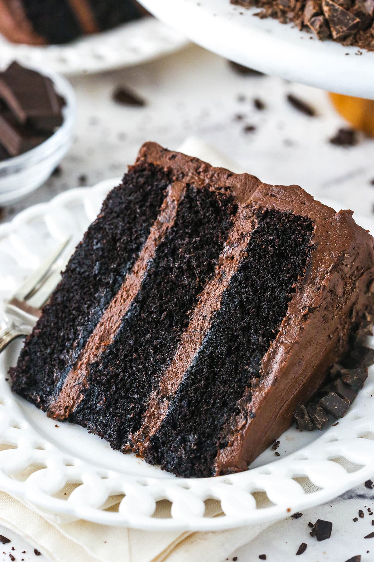 slice of Devil's Food Cake on white plate with another slice in the background on a marble table