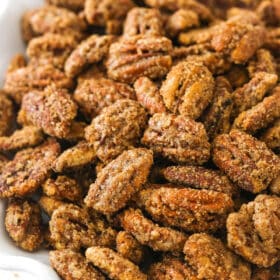A close-up shot of cinnamon sugar pecans in a white bowl with a wavy rim