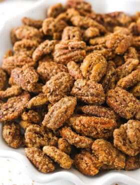 A close-up shot of cinnamon sugar pecans in a white bowl with a wavy rim