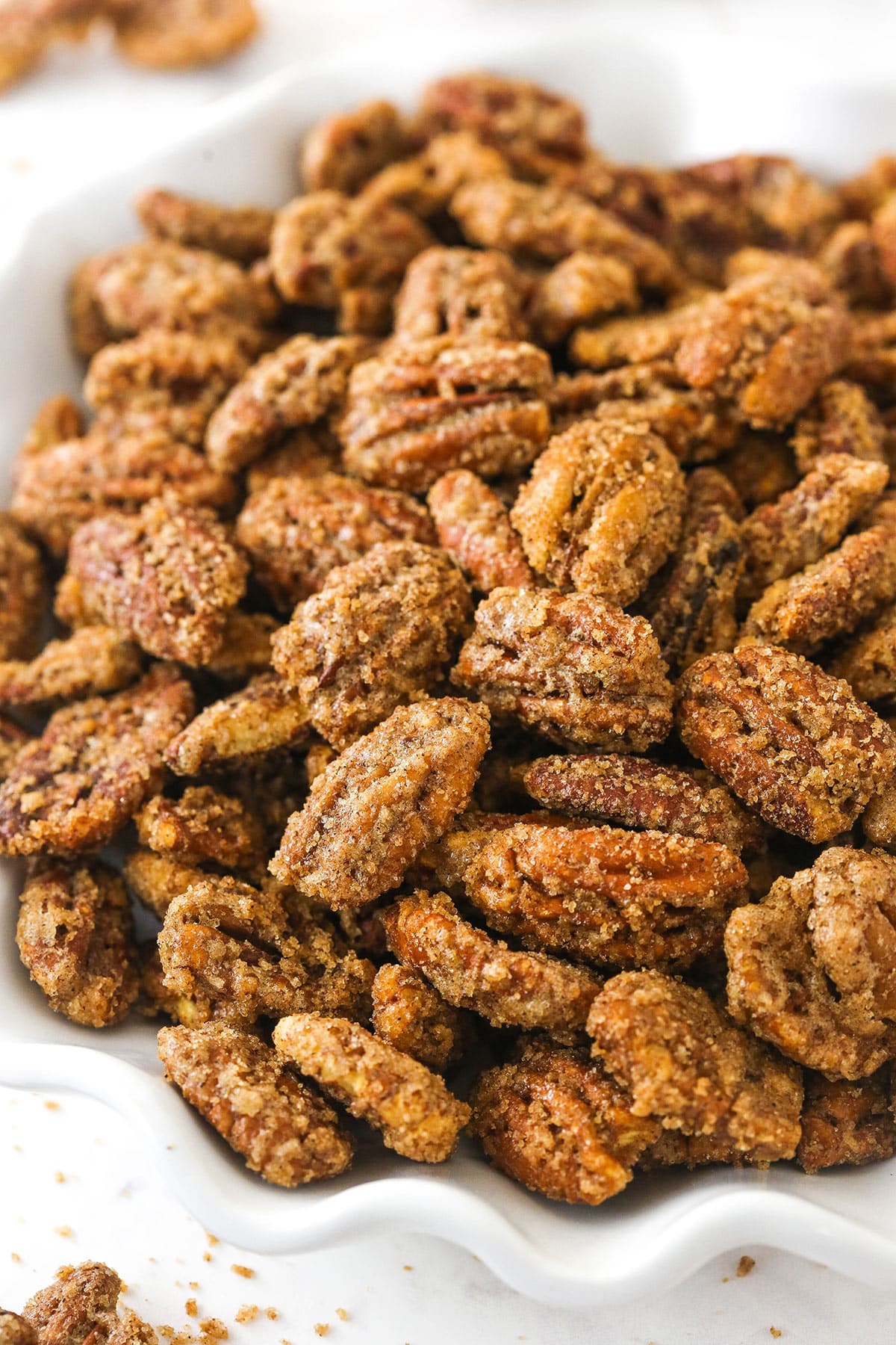 A close-up shot of cinnamon sugar pecans in a white bowl with a wavy rim