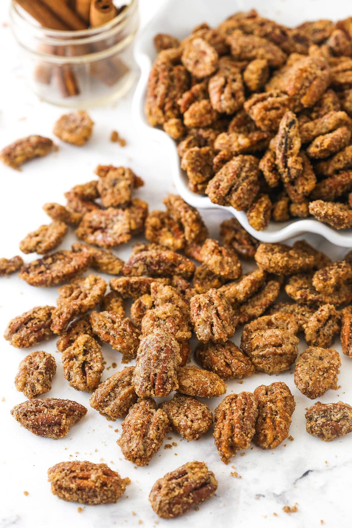 A bunch of candied pecans in a bowl with more spilling out onto a kitchen countertop.