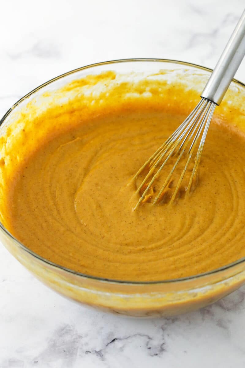 Pumpkin cake batter in a glass mixing bowl with a metal whisk inside.
