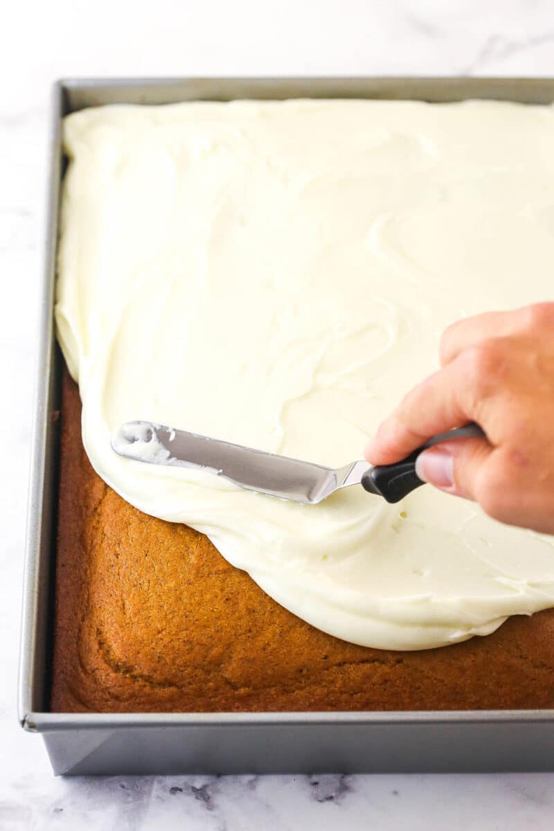 Cream cheese frosting being spread over the top of a cake.
