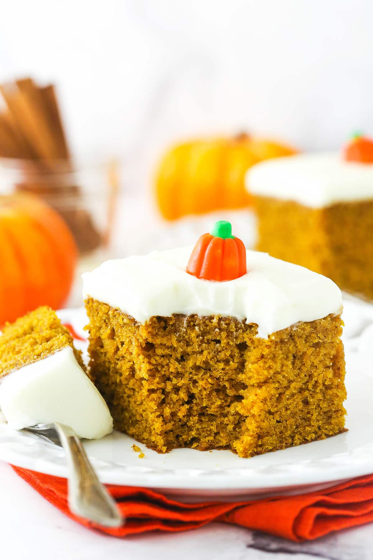 A piece of pumpkin cake on a plate with one bite on a metal dessert fork.