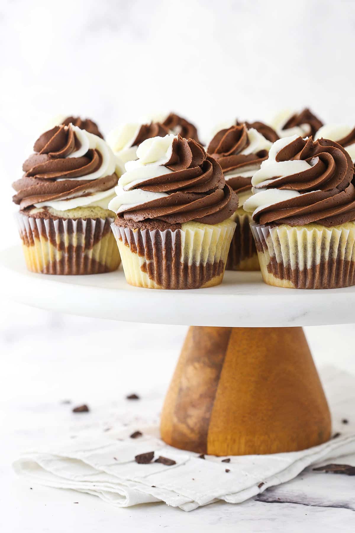 Chocolate and vanilla cupcakes on a cake stand on top of a folded cloth napkin