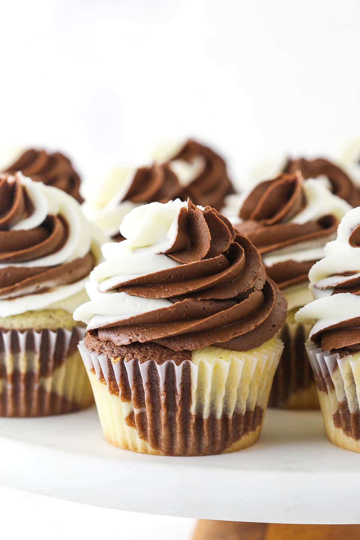 A batch of marble cupcakes on a wooden cake stand with a plastic platform