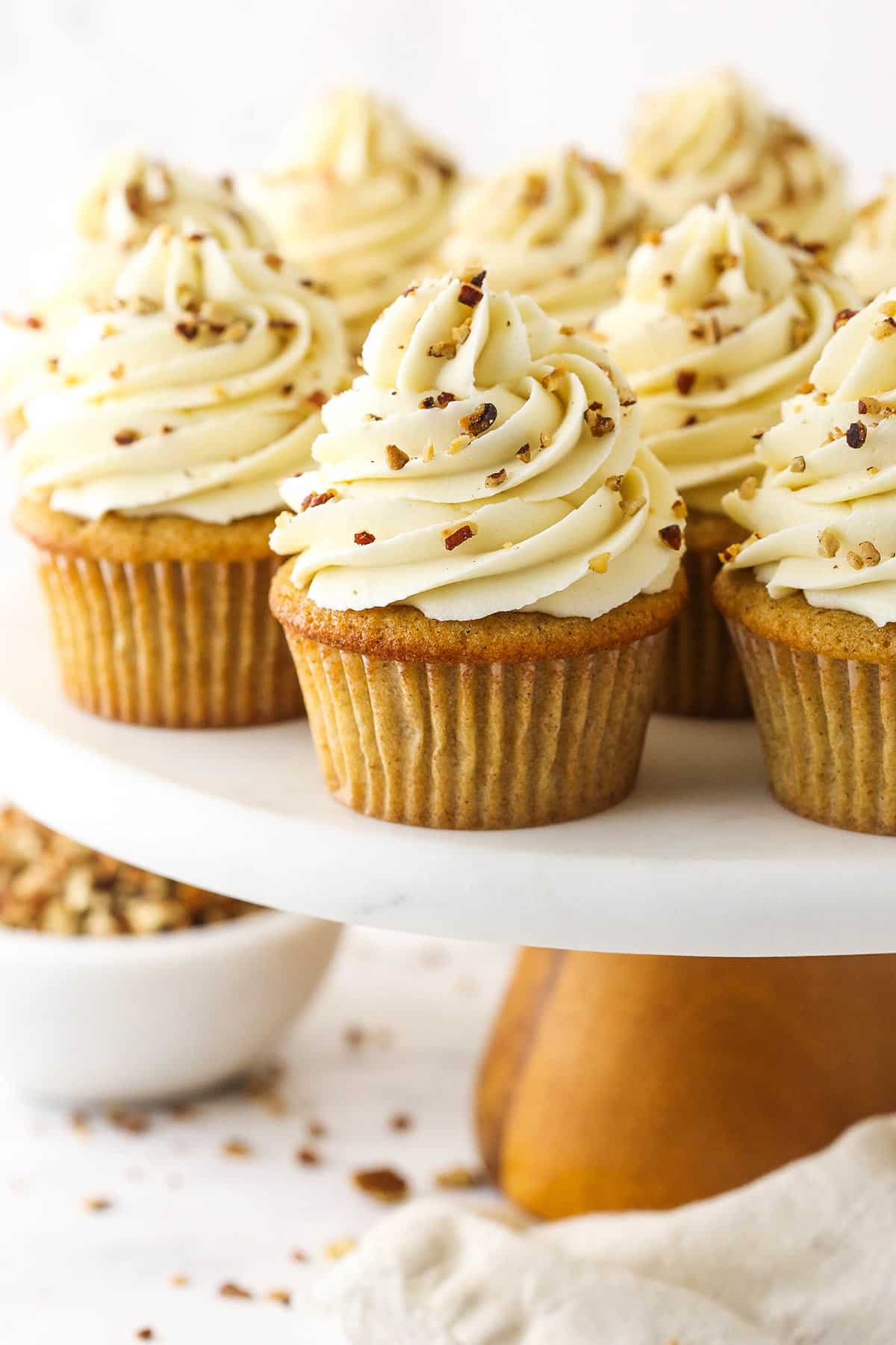 A batch of pecan pie cupcakes on a plastic cake stand with a wooden base