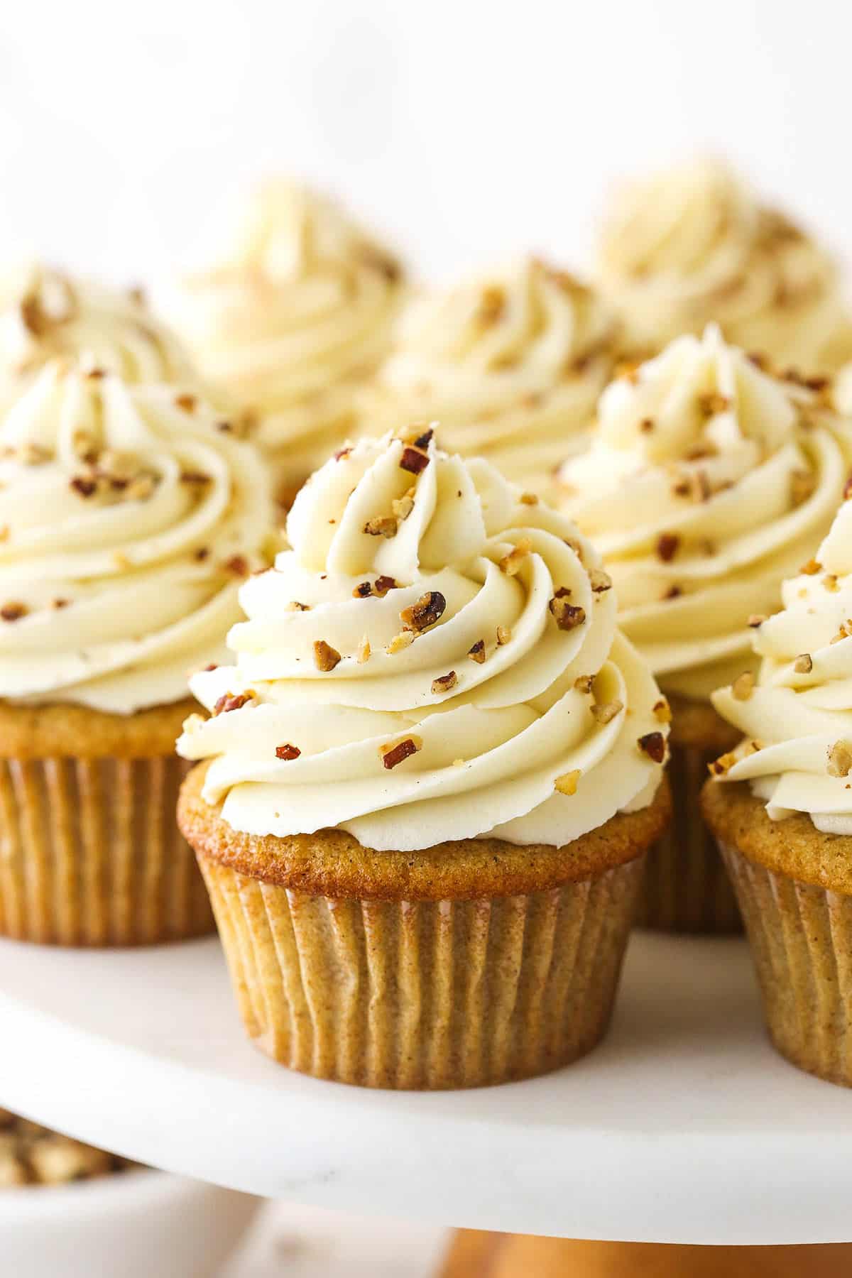 A batch of homemade cupcakes garnished with toasted and chopped pecans on a cake stand