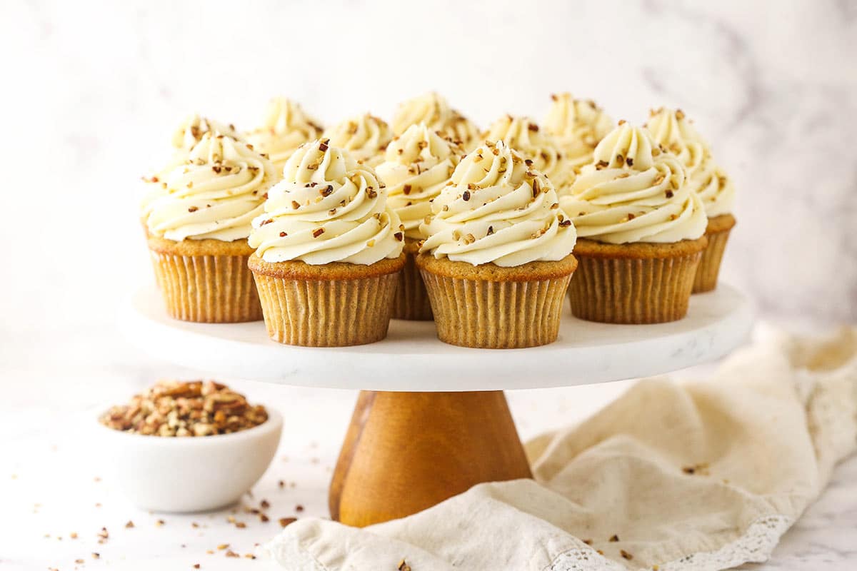 A cake stand on a countertop with pecan cupcakes on top of it and a cream-colored dishtowel beneath it