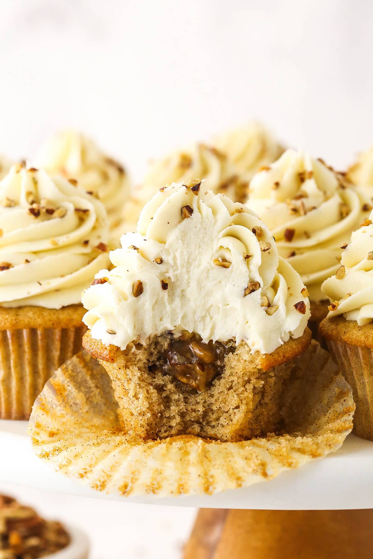 Soft brown sugar cupcakes are stuffed with gooey pecan pie filling & topped with creamy pecan pie frosting in this decadent homemade dessert. An unwrapped pecan pie cupcake with a bite taken out of it to reveal the gooey filling