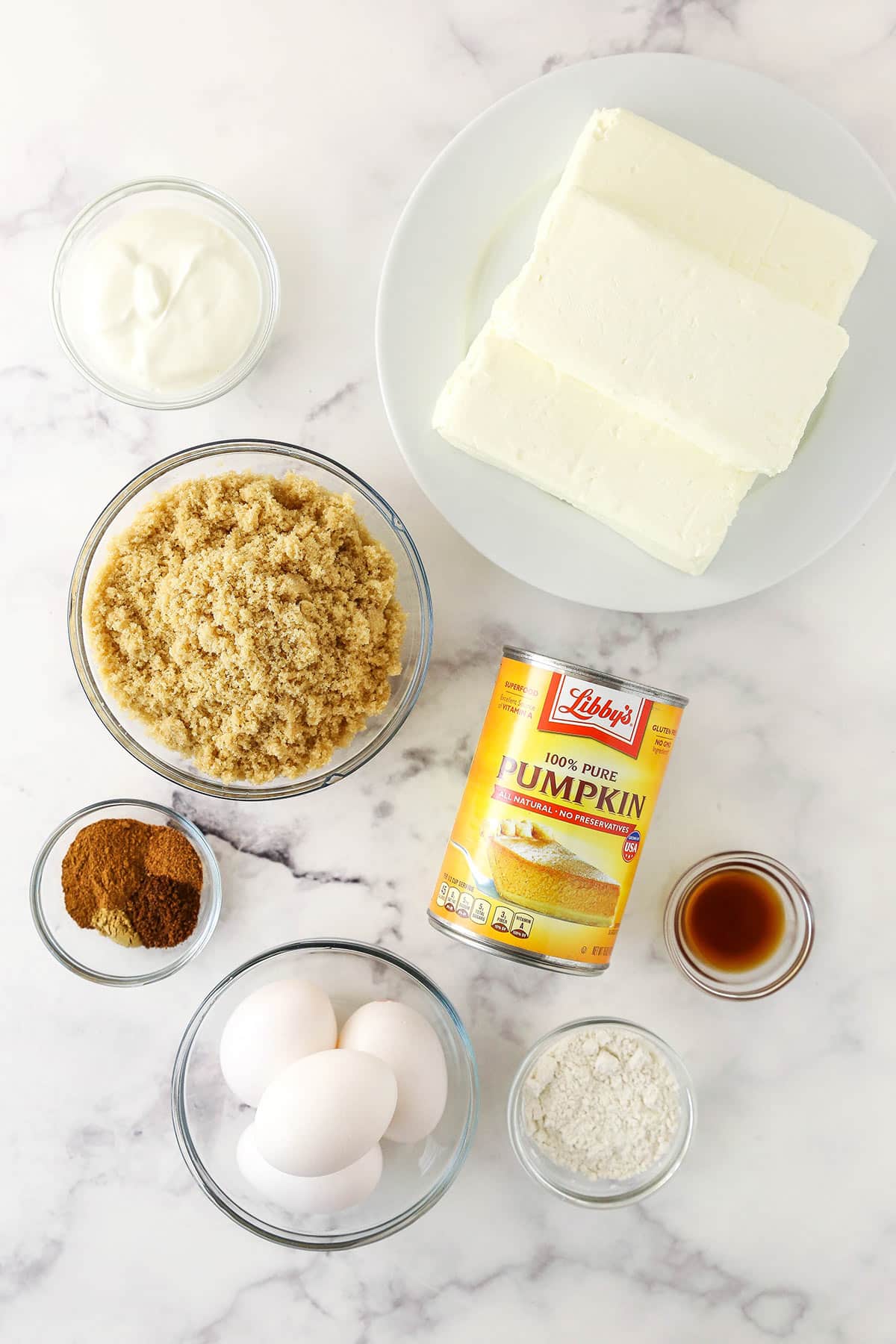 Cream cheese, eggs, vanilla and the rest of the cheesecake ingredients on a marble countertop