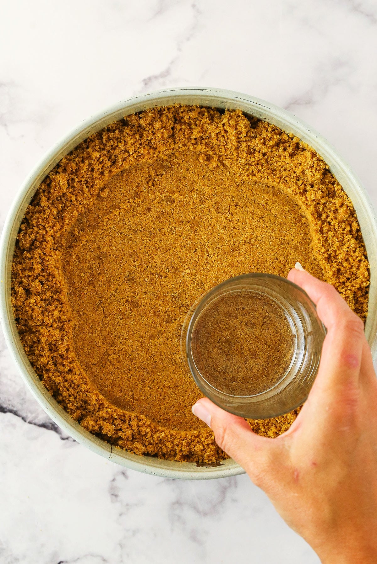 The bottom of a glass being used to press the crust mixture into the pan