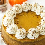 A pumpkin cheesecake on a cake stand beside two small pumpkins
