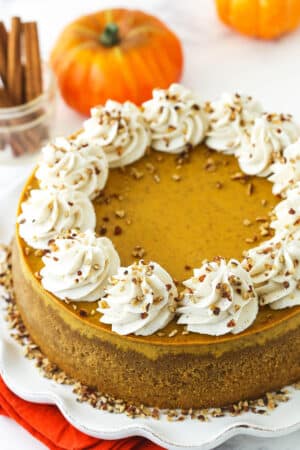 A pumpkin cheesecake on a cake stand beside two small pumpkins