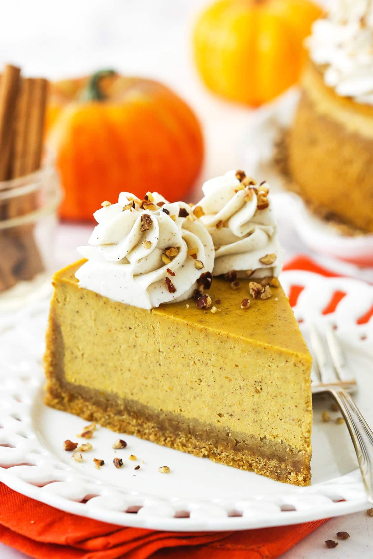 This thick and creamy Pumpkin Cheesecake features a buttery graham cracker crust and fluffy swirls of whipped cream cheese frosting! A slice of cheesecake on a plate with homemade whipped cream and chopped pecans on top